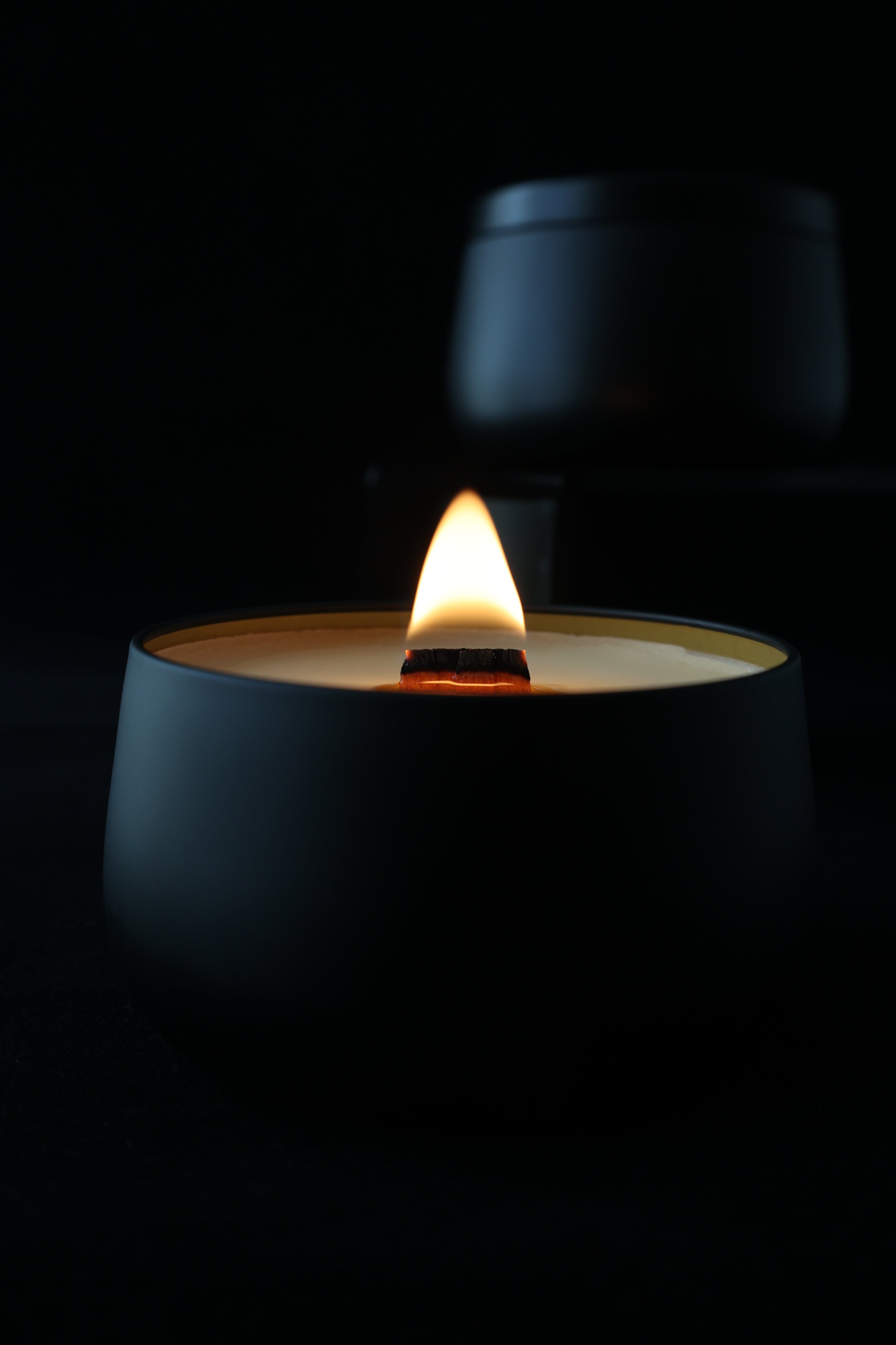Lit candle in a black tin against a black background