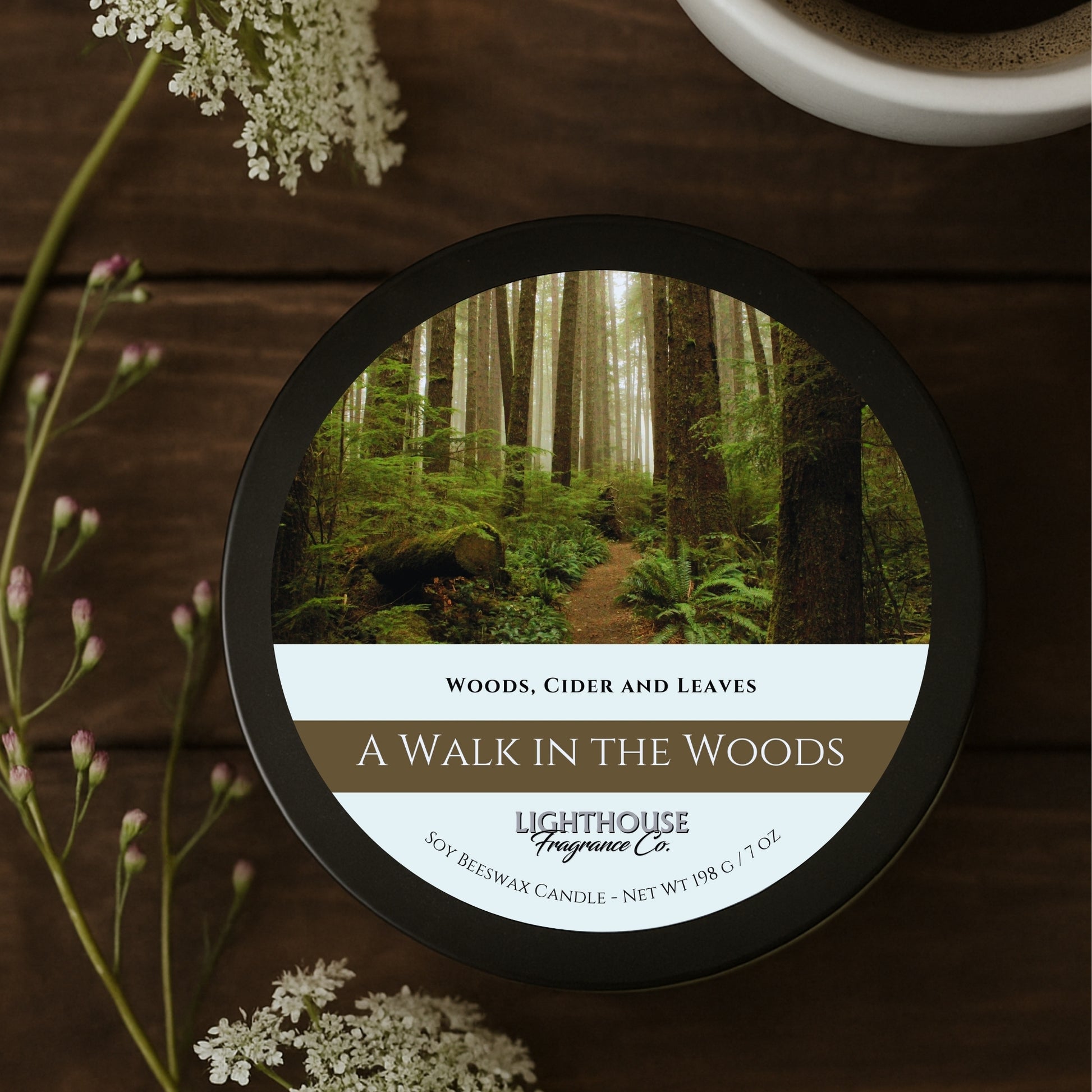 Candle labeled 'A Walk in the Woods' by Lighthouse Fragrance Co. on a wooden surface with flowers.