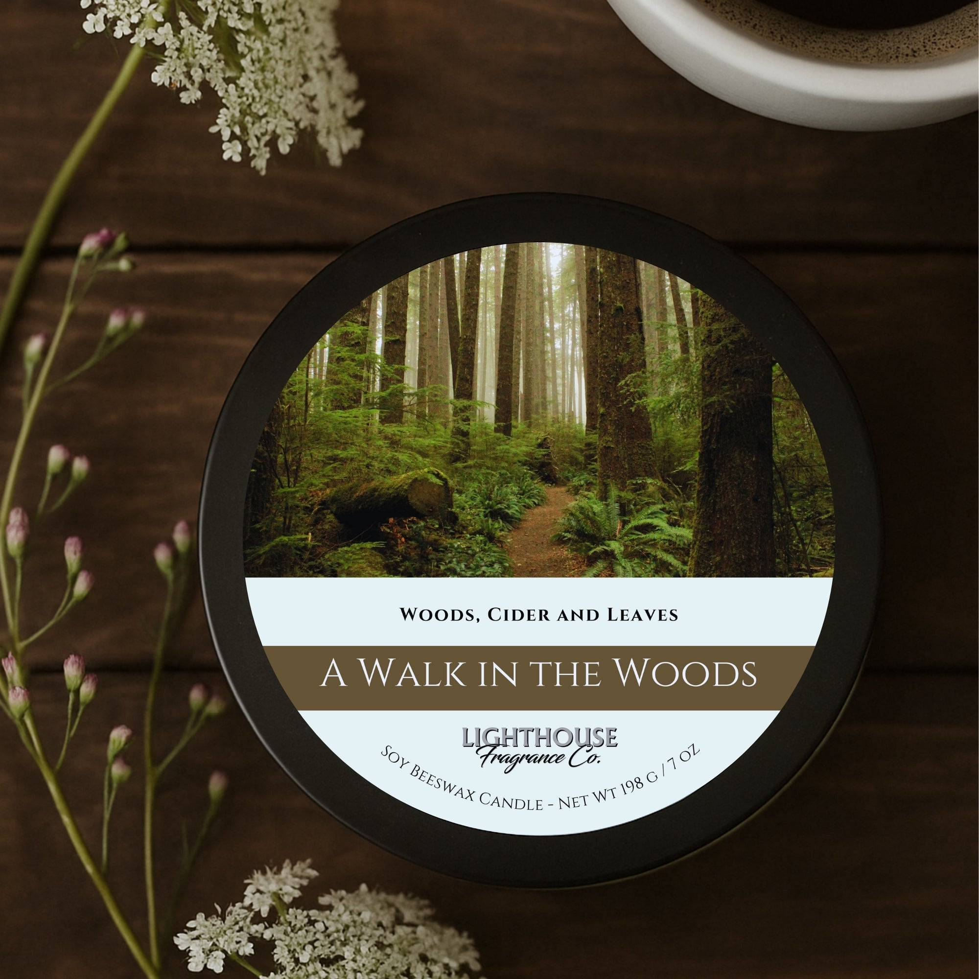 Candle labeled 'A Walk in the Woods' by Lighthouse Fragrance Co. on a wooden surface with flowers.