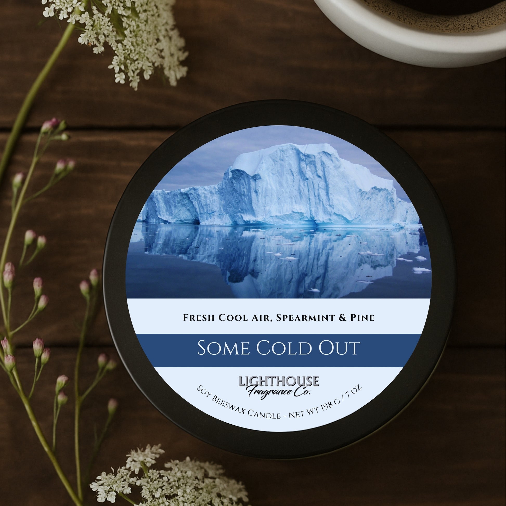 Candle jar labeled 'Some Cold Out' by Lighthouse Fragrance Co. on a wooden surface with flowers.