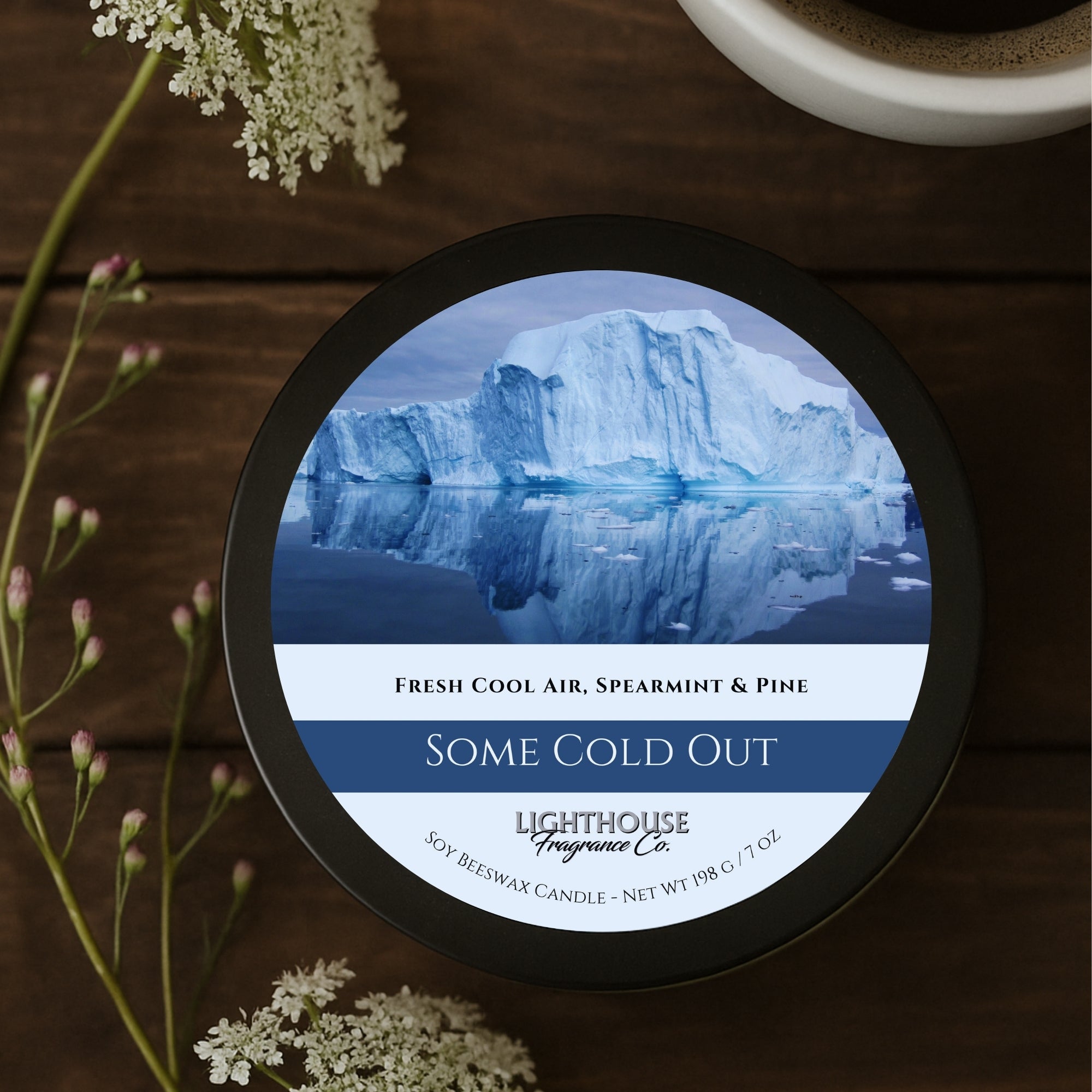 Candle jar labeled 'Some Cold Out' by Lighthouse Fragrance Co. on a wooden surface with flowers.