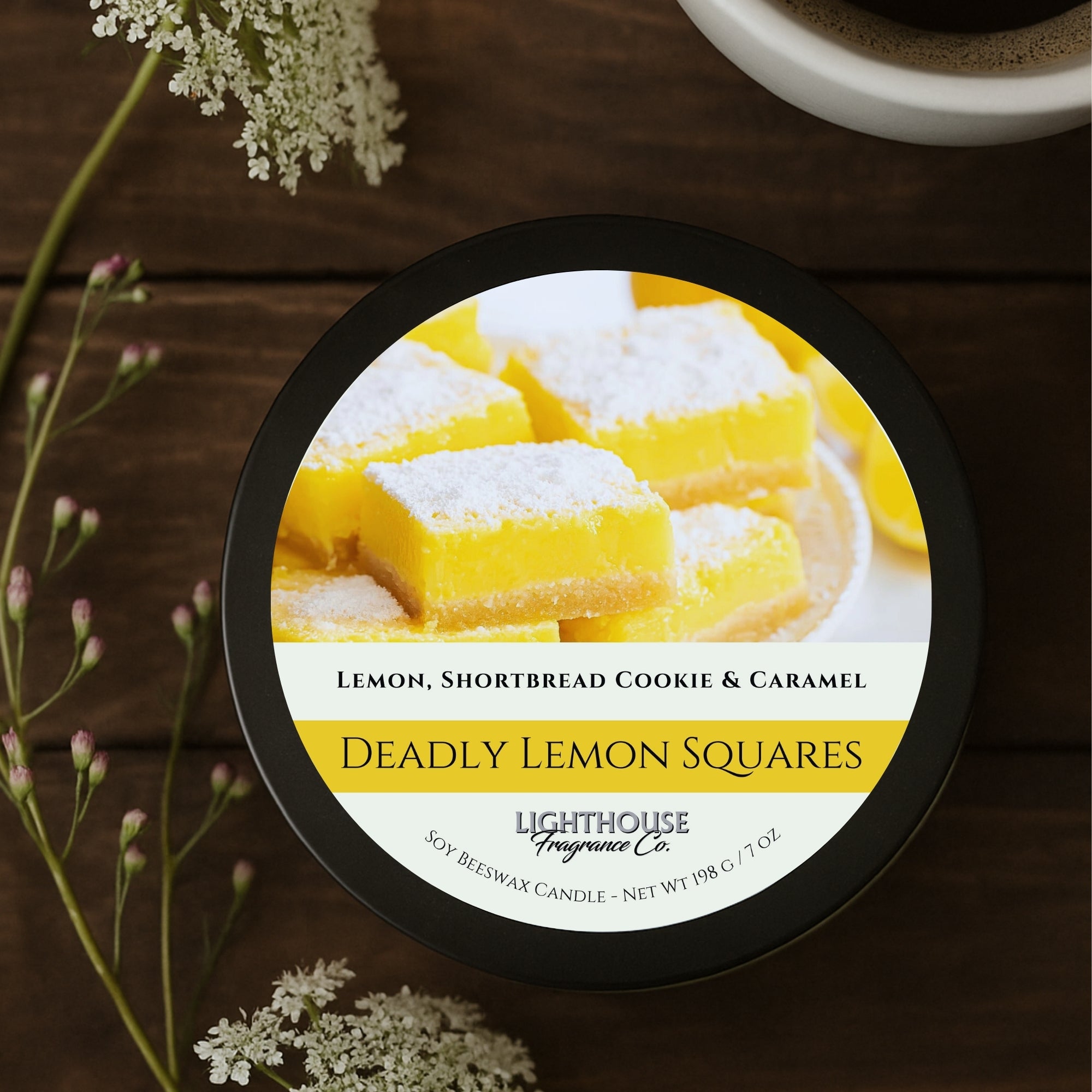 Lighthouse Fragrance Co. candle labeled 'Deadly Lemon Squares' on a wooden surface with flowers.