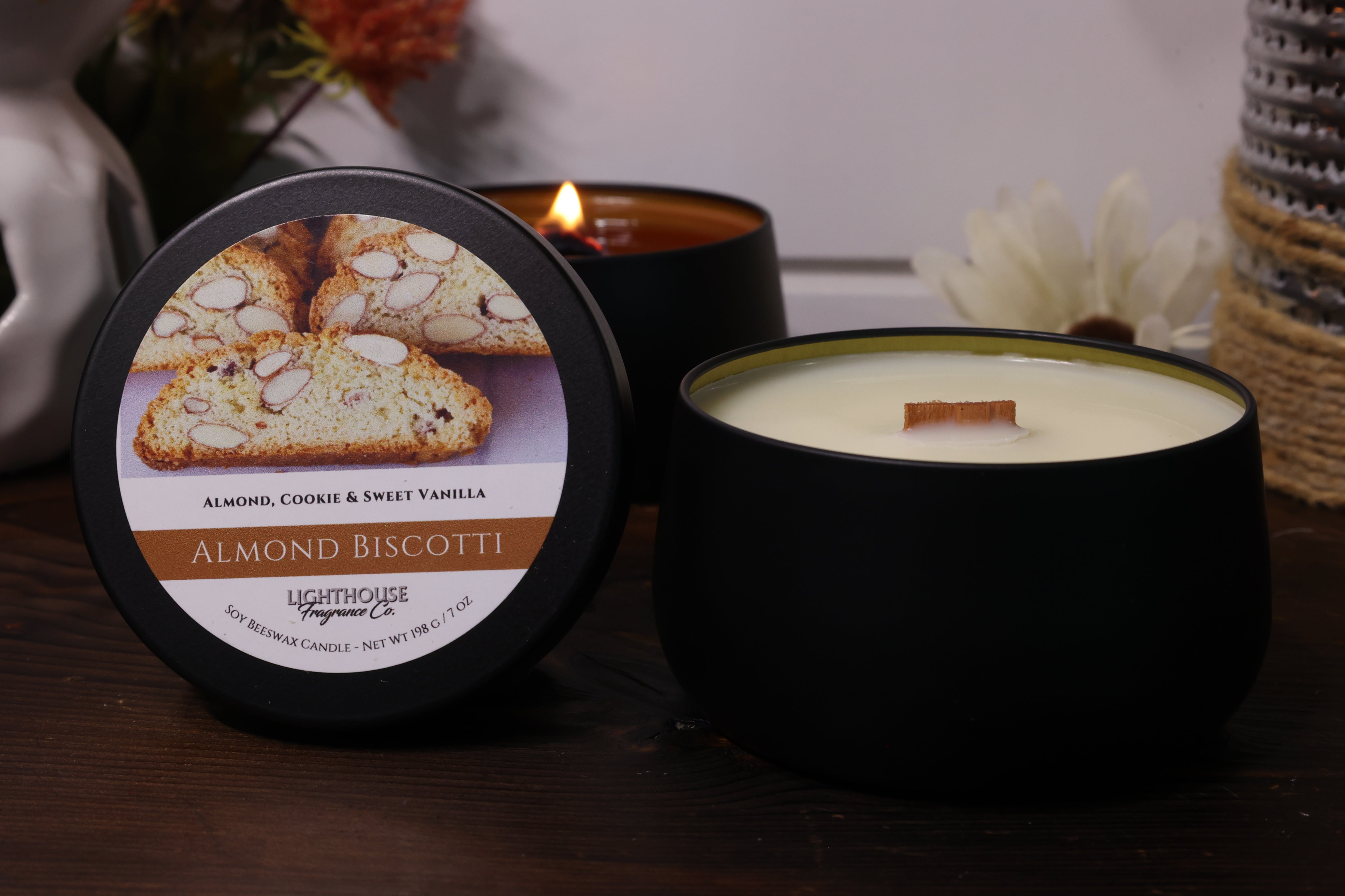Black candle with a label featuring almond biscotti on a wooden surface.