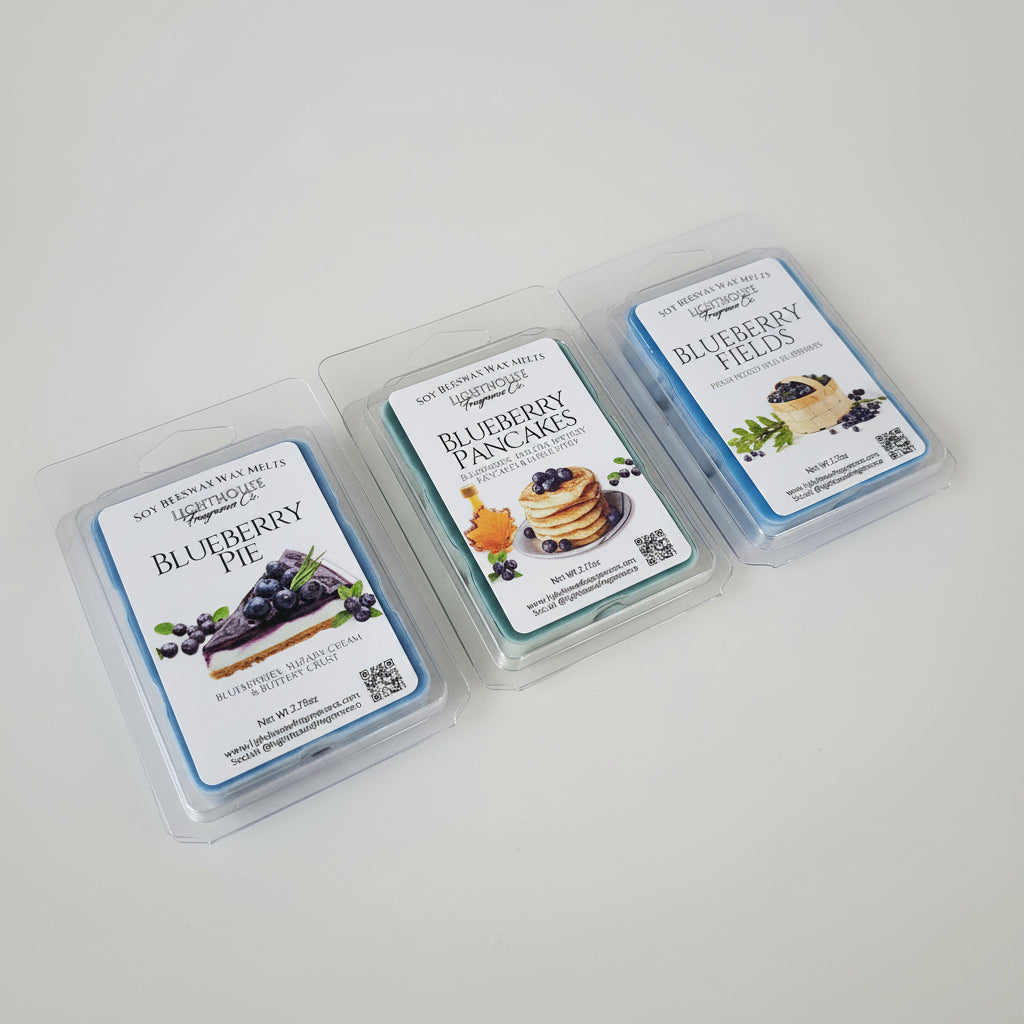 Three wax melts in clear clamshell packaging on a white surface. The labels read Blueberry Pie, Blueberry Pancakes, and Blueberry Fields, with blueberry-themed food photography on the front.