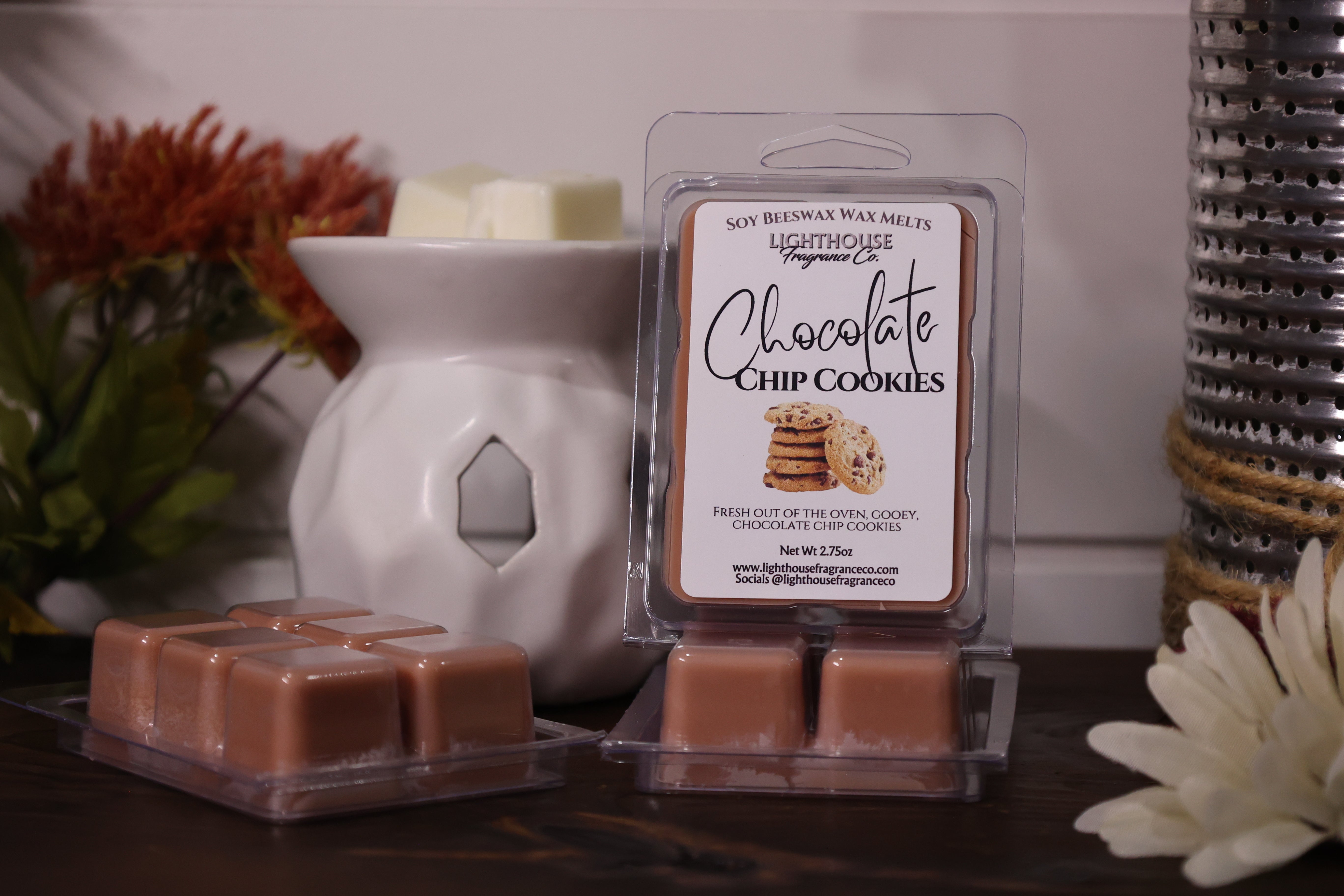 Packaged wax melts labeled 'Chocolate Chip Cookies' with a white wax warmer and decorative items.
