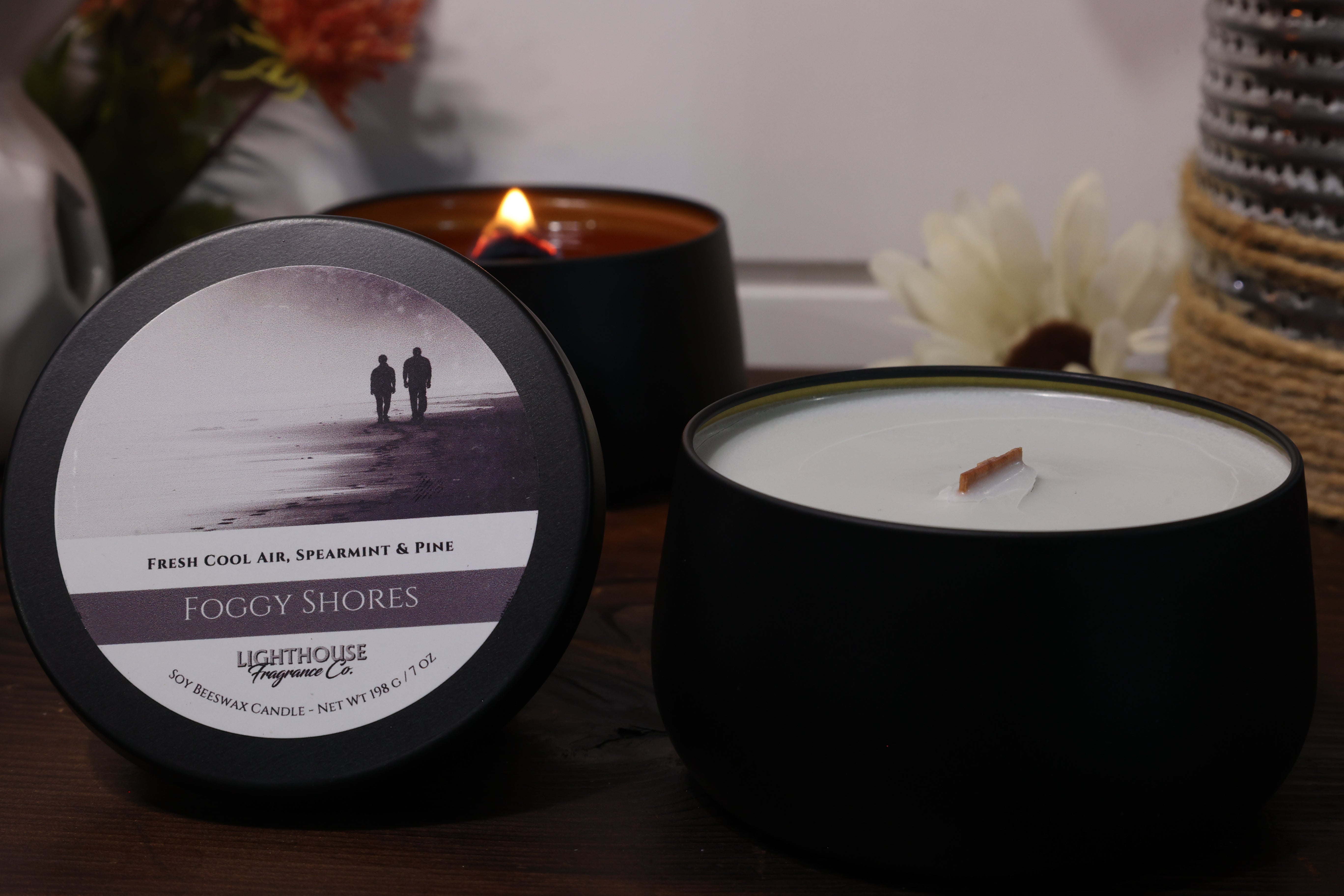 Candle with 'Foggy Shores' label and another candle in the background on a wooden surface.