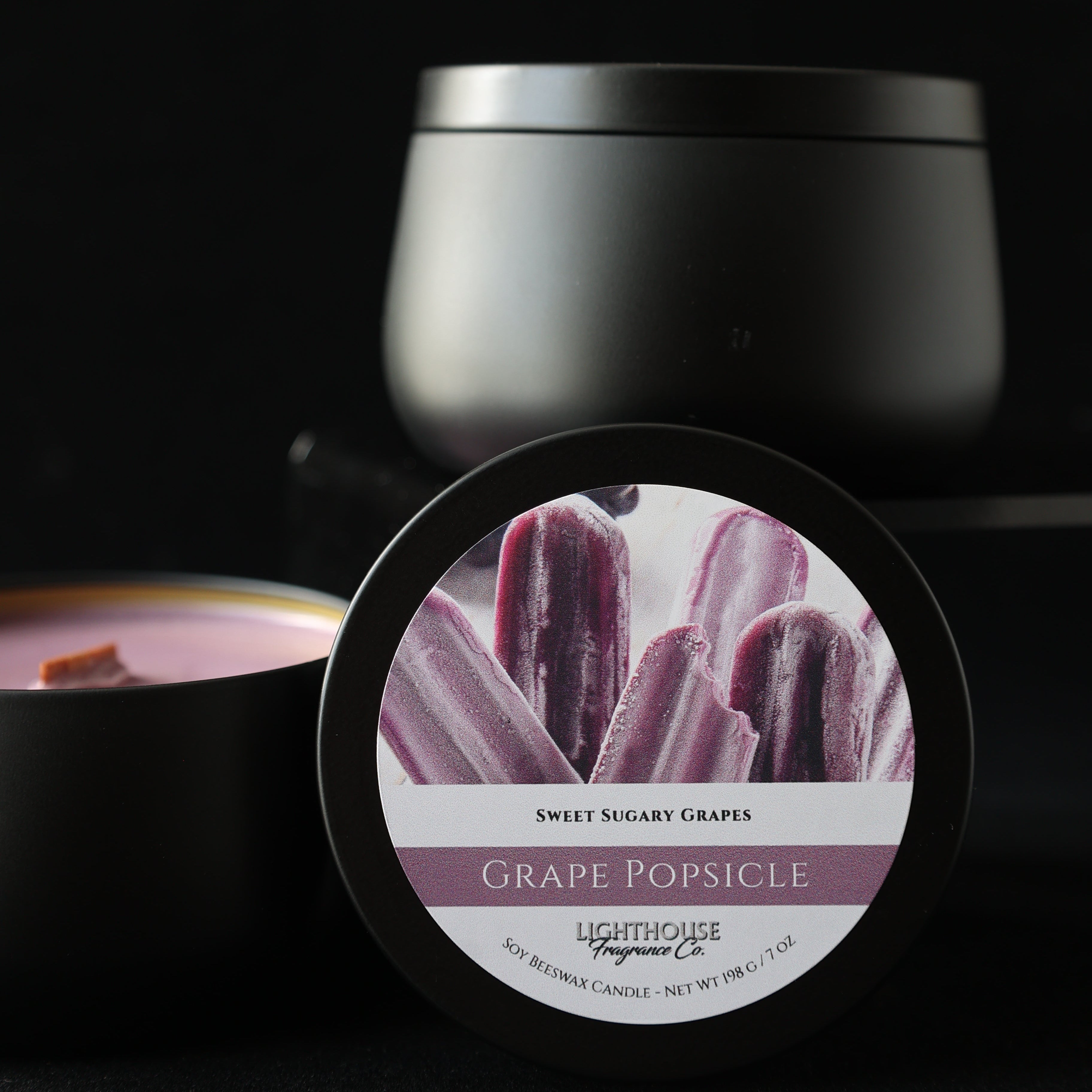 Grape popsicle candle in a black tin against a black background