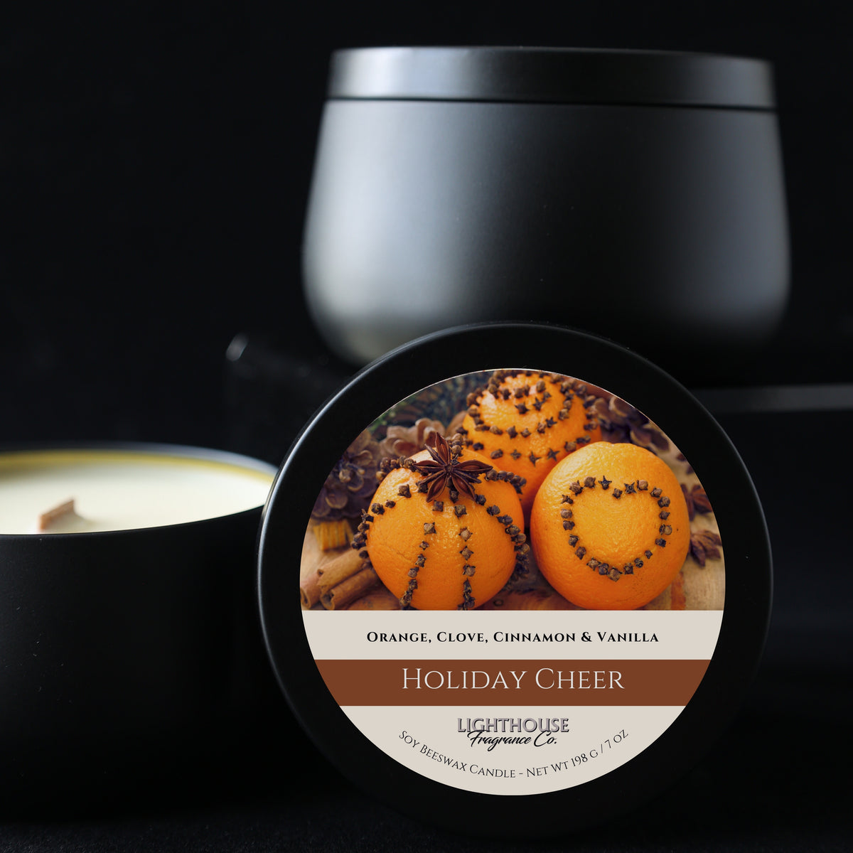 Candle with a 'Holiday Cheer' label featuring oranges and spices, set against a dark background.