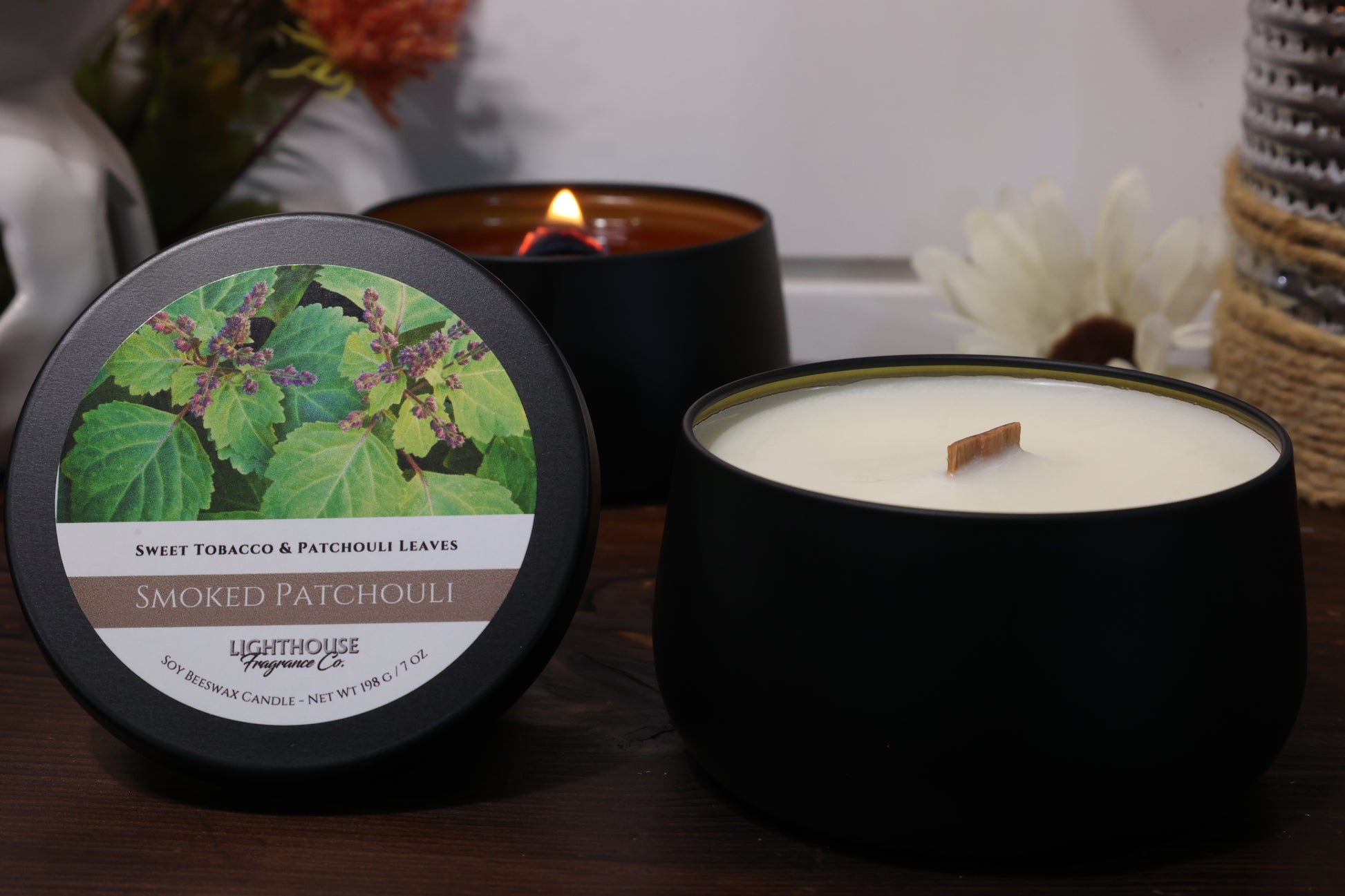 Two candles, one lit and one unlit, with a decorative label on a wooden surface.