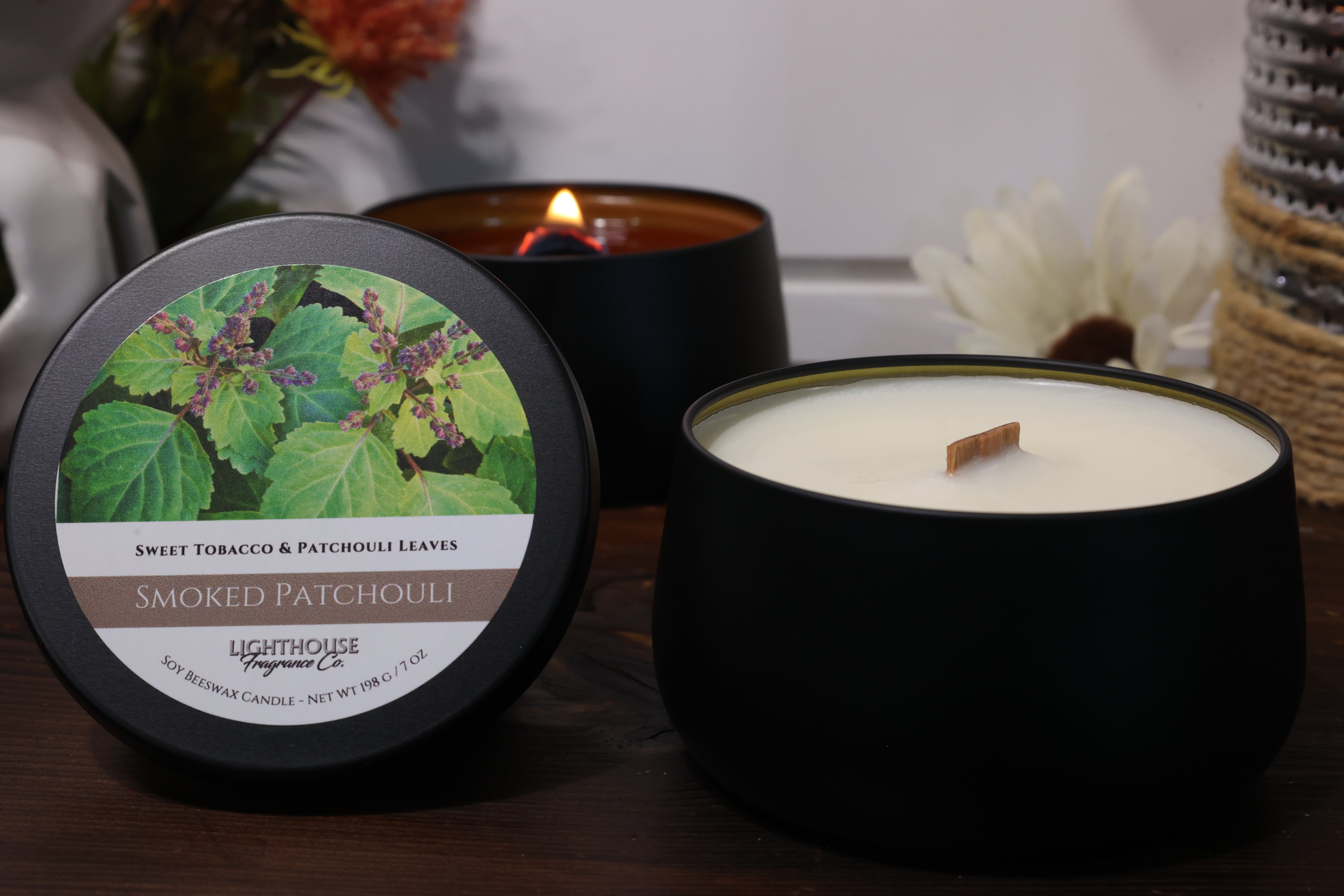Two candles, one lit and one unlit, with a decorative label on a wooden surface.