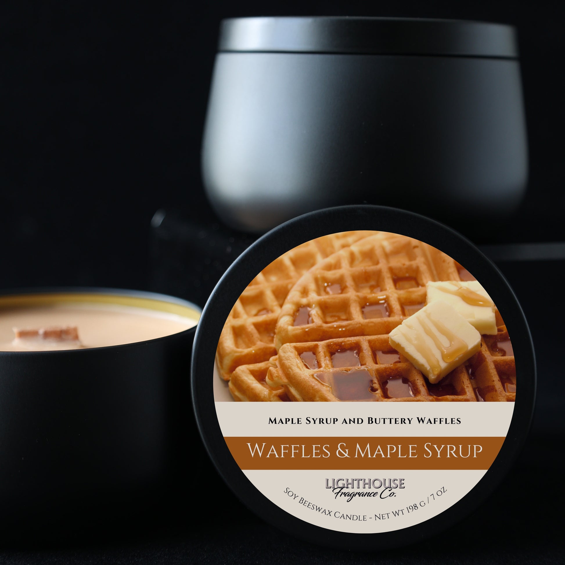 Candle with a waffles and maple syrup label in front of a black container.