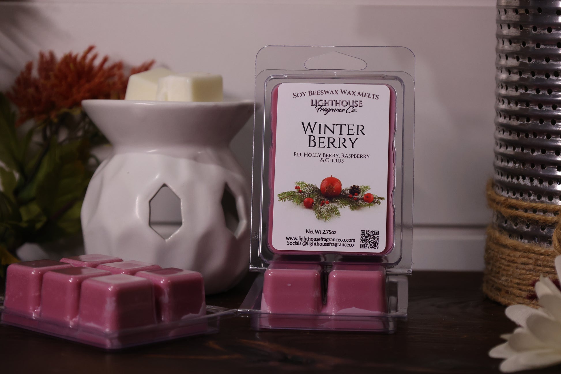 Packaged wax melts labeled 'Winter Berry' next to a wax warmer on a wooden surface.
