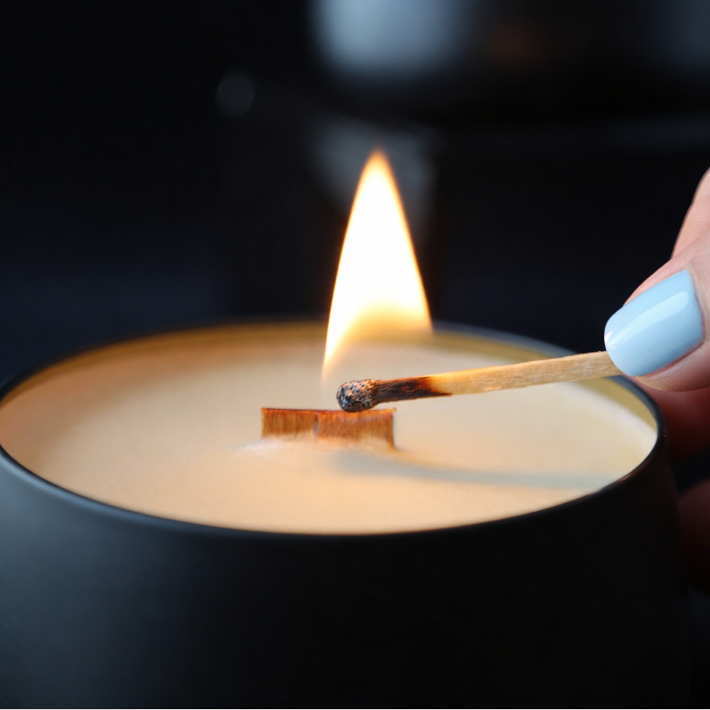 Person lighting a candle with a match against a dark background